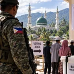 A voter casting a ballot at a Bangsamoro polling station while security personnel stand nearby