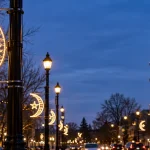 Editorial illustration of crescent-and-star street lighting along a city boulevard at dusk.