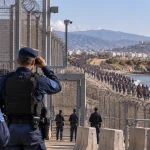 Illustration of European border authorities monitoring a large movement of migrants approaching a fortified coastal frontier.