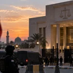 Editorial illustration of a guarded Iraqi courthouse with French and Iraqi flags representing upcoming trials of French Islamic State suspects.
