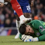 Illustration of a football goalkeeper on the ground as an opposing player's raised boot makes contact near his head during a crowded challenge.