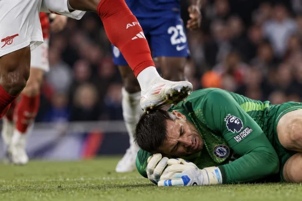 Illustration of a football goalkeeper on the ground as an opposing player's raised boot makes contact near his head during a crowded challenge.