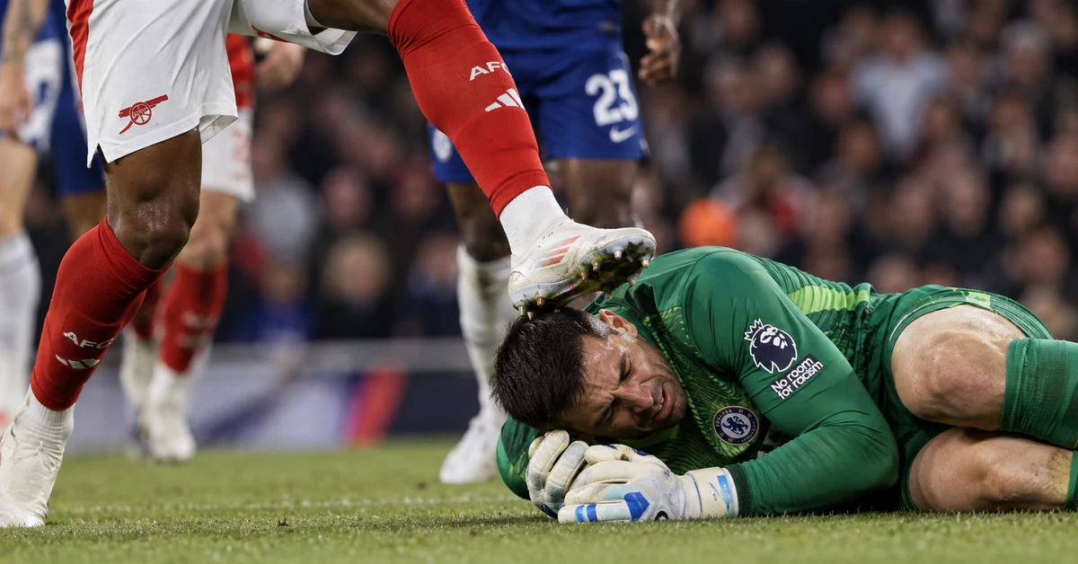 Illustration of a football goalkeeper on the ground as an opposing player's raised boot makes contact near his head during a crowded challenge.