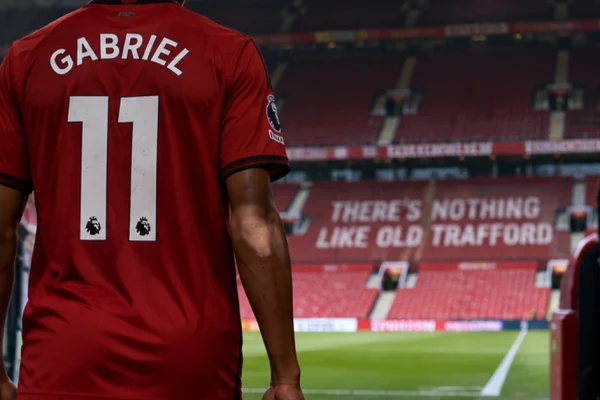 A young footballer in red walking towards the pitch from a stadium tunnel, illustrating JJ Gabriel's request to leave Manchester United.