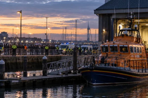Illustration of a lifeboat station at Portsmouth harbour with a rescue vessel alongside while police monitor a crowd across the marina.