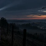 Editorial illustration of a drone approaching a guarded border area at dusk, with radar equipment and a railway visible nearby.